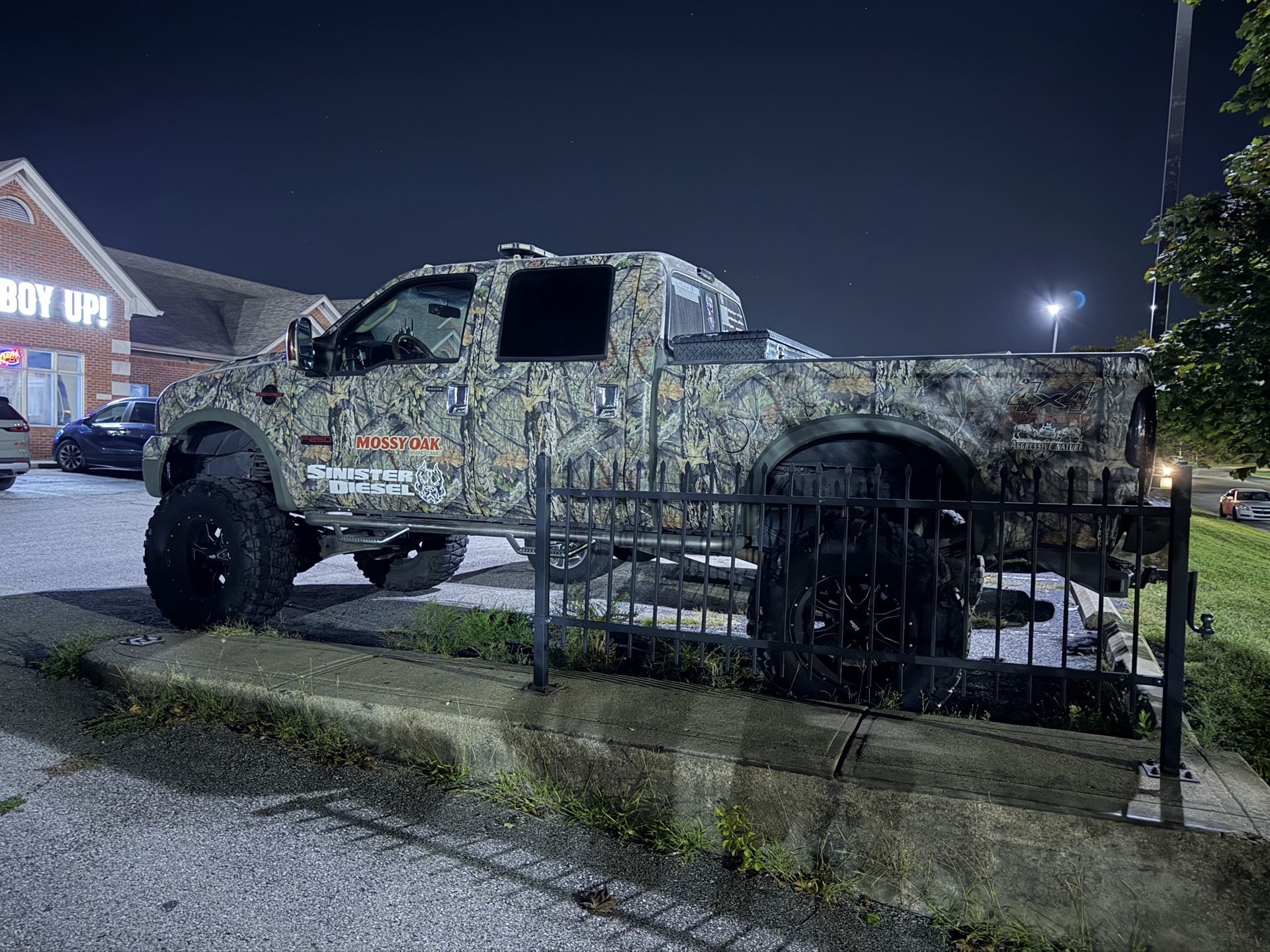 A camo-wrapped lifted truck spotted outside a store at night